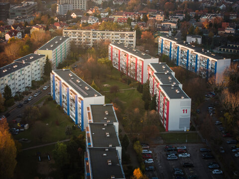 Aerial view of blocky apartment buildings with vibrant pops of red and blue paint amid a sea of autumnal trees in Suchanino neighborhood, Gdansk, Pomorskie, Poland.