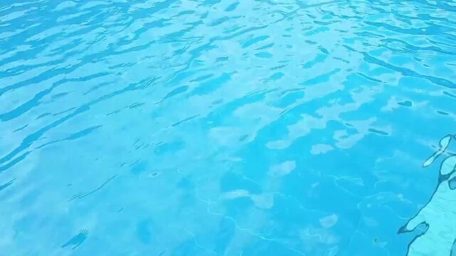 Vibrant blue pool water with ripples meeting gray stone coping. Summer leisure, abstract background, clear water texture. High-angle