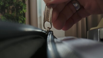 A Macro shot of a hand unzipping a suitcase with a plastic zipper and metal pull tab in a brightly lit room.