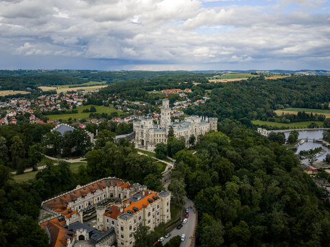 Aerial view of the majestic Zamek Hluboka castle with its white facade rising above the dense green forests under a cloudy sky, Hluboka nad Vltavou, Jihocesky kraj, Czechia.