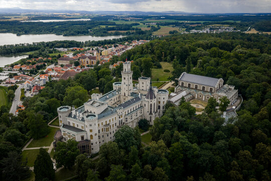 Aerial view of the striking Zamek Hlubok&aacute; castle, its white facade and towers piercing the lush green forest canopy, Hluboka nad Vltavou, Jihocesky kraj, Czechia.