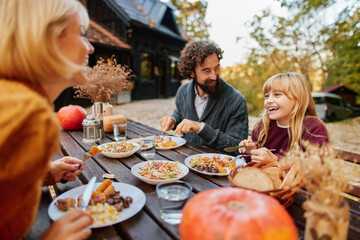 A happy family gathers around a wooden table during autumn, sharing a meal filled with laughter, vibrant meals, and a warm atmosphere surrounded by nature.