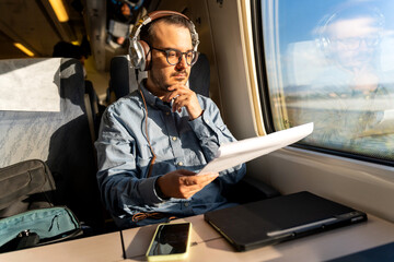 Man wearing headphones reading document on train journey