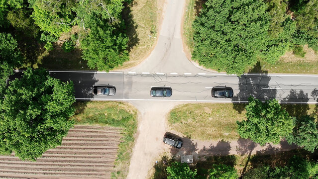 Cars driving on a rural road intersection, overhead view showing traffic and green nature landscape