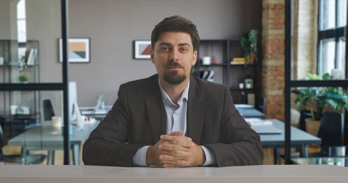 A man in a suit sits confidently in a professional live streaming studio setup, ready to broadcast in a modern office setting.