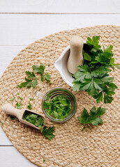 Above view of homemade herbal medicinal tea made from parsley Petroselinum crispum. Green leaves in tea cup on white wood background with fresh leaves in mortar and pestle.