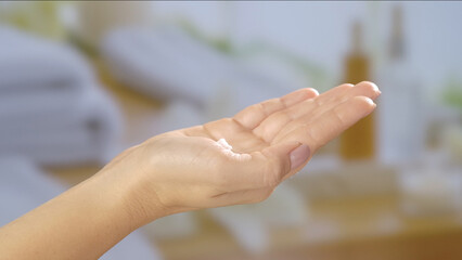 Close up of an open hand holding a small amount of cream, set against a blurred spa like background. Beauty concept, skin care, and cream product presentation.