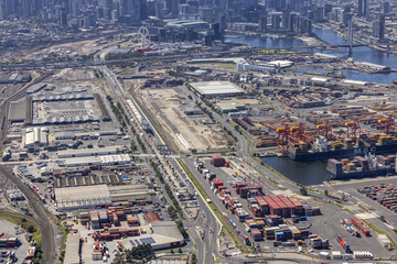 West Melbourne, Australia - 07 February 2022: Aerial view of a bustling port where cargo containers and ships meet the city's skyline under a blanket of soft, diffused sunlight.