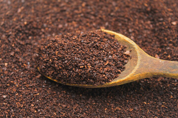 Close-up of dark brown coffee grounds on a spoon. The coffee grounds appear fine to slightly coarse.