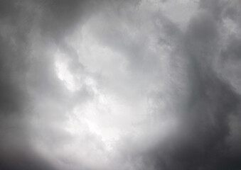 A dramatic stormy sky where the center forms a bright circular opening surrounded by thick, dark clouds, creating a powerful contrast between light and shadow.
