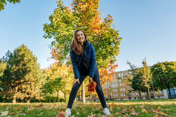 Young woman playing with autumn leaves in a city park at golden hour, full-length portrait