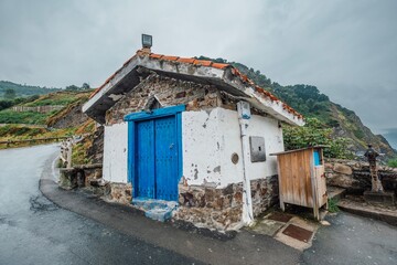 Small Rustic Stone Building with Bright Blue Door on Rainy Coastal Road