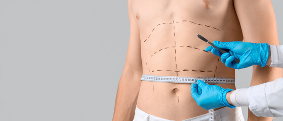 Plastic surgeon with scalpel measuring man's abdomen on grey background, closeup