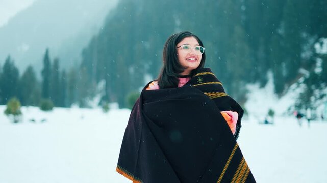 Woman enjoys snowfall in mountains. Cold winter days in Himalayas at Aru valley, Jammu and Kashmir, India. Indian female traveler enjoying scenic nature view during holidays. Travel concept.
