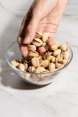 Close up of female hand grabbing pistachio nuts from a bowl