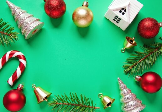 Flat lay of red and gold baubles, candy cane, glitter trees, white ceramic house, fir sprigs and tiny bells on green background - Powered by Adobe