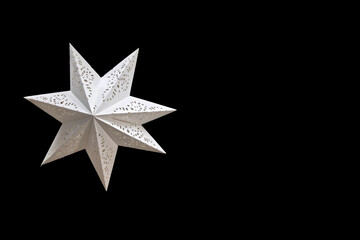 White decorative star on black background. Isolated white decorative star with cutout patterns on a black background. Elegant geometric Christmas ornament, festive minimalist decoration.