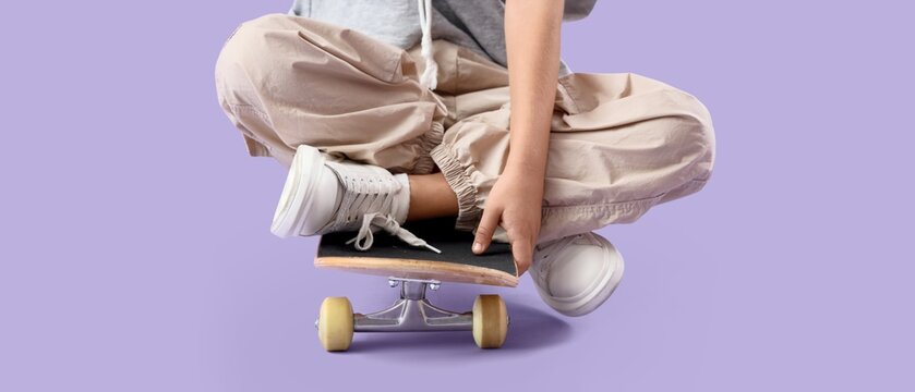 Little boy sitting on skateboard against lilac background - Powered by Adobe