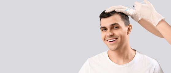 Young man receiving injection for hair growth on light background with space for text