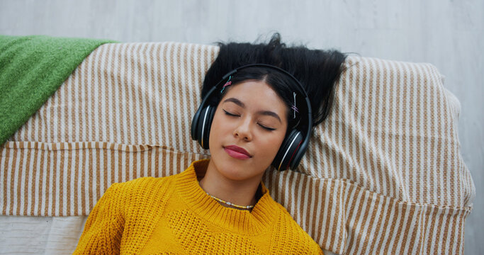 Home, above and woman with headphones, relax and listening to music, sleeping and sound. Apartment, audio and person with break, resting and playlist album with radio, comfort and podcast with song