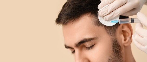Fototapeta premium Young man receiving injection for hair growth on beige background with space for text, closeup