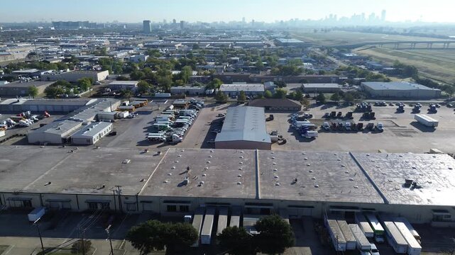 Industrial freight zone west of Trinity River Trail featuring rows of semi-trailers, distribution buildings, warehouse hub, and organized vehicle flow and skyline anchoring the urban horizon