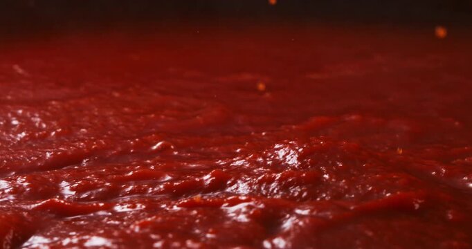 Slow motion close-up of boiling rich red tomato sauce bubbling  naturally under warm light with deep red tones and soft steam at 1000fps. Concept of homemade Italian tradition and culinary passion.