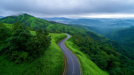 Obraz premium Curved mountain road winding through green forest valley seen from above. 