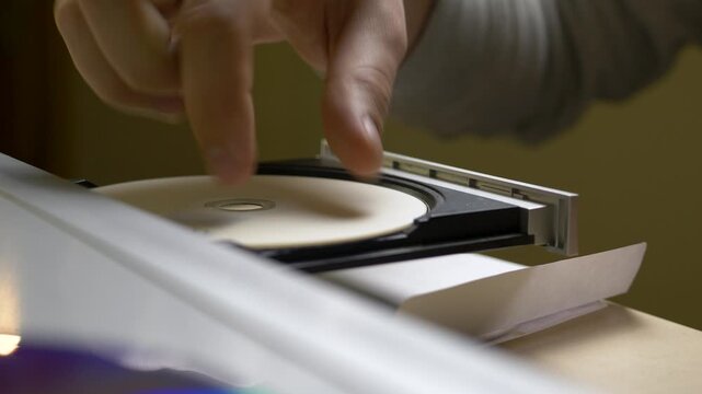 Male hand slides CD into old player kept for memory. Early 2000s music culture. Quiet respect for fading formats. Process of setting up film entertainment and quiet relaxation time