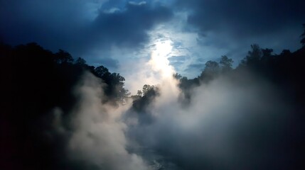 Obraz premium Mist and fog flowing through a valley, trees silhouetted against the dark sky, rays of sun piercing through clouds
