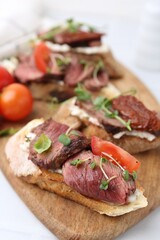 Delicious bruschettas with roast beef served on white table, closeup