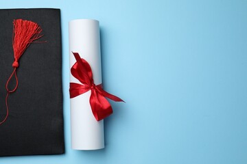 Diploma and graduation hat on light blue background, top view. Space for text