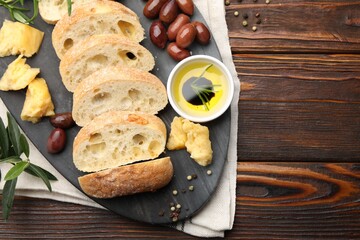 Pieces of fresh ciabatta, oil, olives, cheese and peppercorns on wooden table, flat lay. Space for text