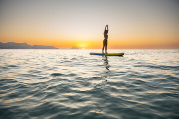 Young woman paddleboarding on calm ocean at sunset