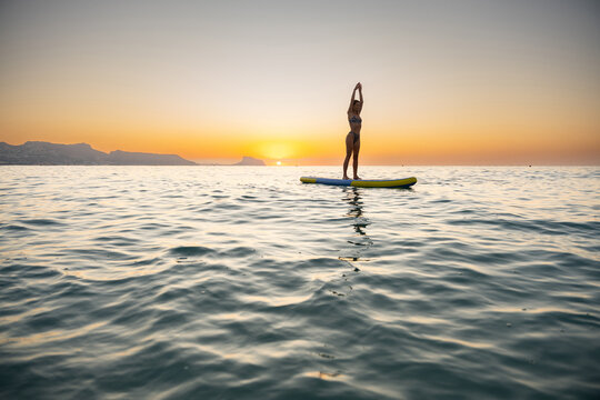 Young woman paddleboarding on calm ocean at sunset