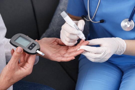 Diabetes. Doctor in medical gloves checking patient's blood sugar level with lancet pen and glucometer on sofa, closeup - Powered by Adobe