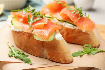 Tasty bruschettas with salmon, cream cheese, cucumber and arugula on table, closeup