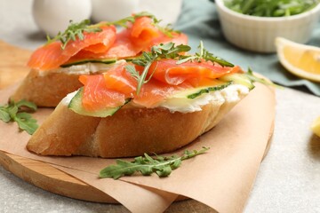 Tasty bruschettas with salmon, cream cheese, cucumber and arugula on grey table, closeup