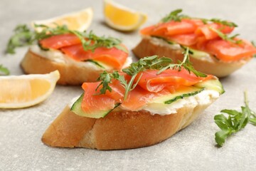 Tasty bruschettas with salmon, cream cheese, cucumber, arugula and lemon on grey table, closeup