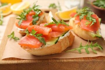 Tasty bruschettas with salmon, cream cheese, cucumber and arugula on table, closeup