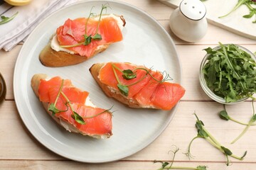 Tasty bruschettas with salmon and cream cheese served on wooden table, flat lay