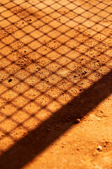 Tennis court surface with shadows creating a pattern at sunset showcasing a vibrant clay texture