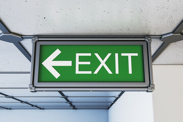 Green exit sign with left arrow mounted on ceiling of modern hallway with industrial design and light background, symbolizing emergency route. 3D Rendering