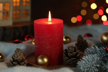 Burning candle, cones, fir tree branches and baubles on light blanket against black background with blurred lights, closeup. Bokeh effect