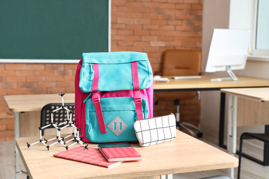 Colorful school backpack with stationery and molecular model on desk in classroom - Powered by Adobe
