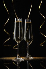 Happy New Year. Sparkling wine in flute glasses and serpentine streamers on black background