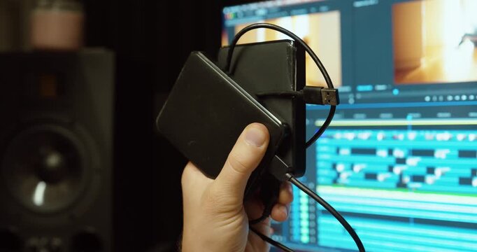A video editor holds multiple hard drives while working in Adobe Premiere Pro. Concept of data storage, media overload, and digital workflow challenges.