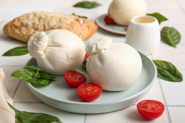 Plate of tasty Burrata cheese with basil and tomatoes on white tile table