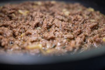 Close-up of minced beef sizzling with onions in a hot pan. The shallow depth of field and blurred foreground offer excellent copy space for culinary blogs and recipe concepts.