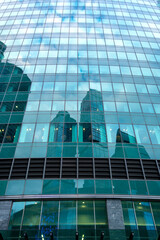Vertical scene with glass panels reflecting nearby buildings and a cloudy sky.